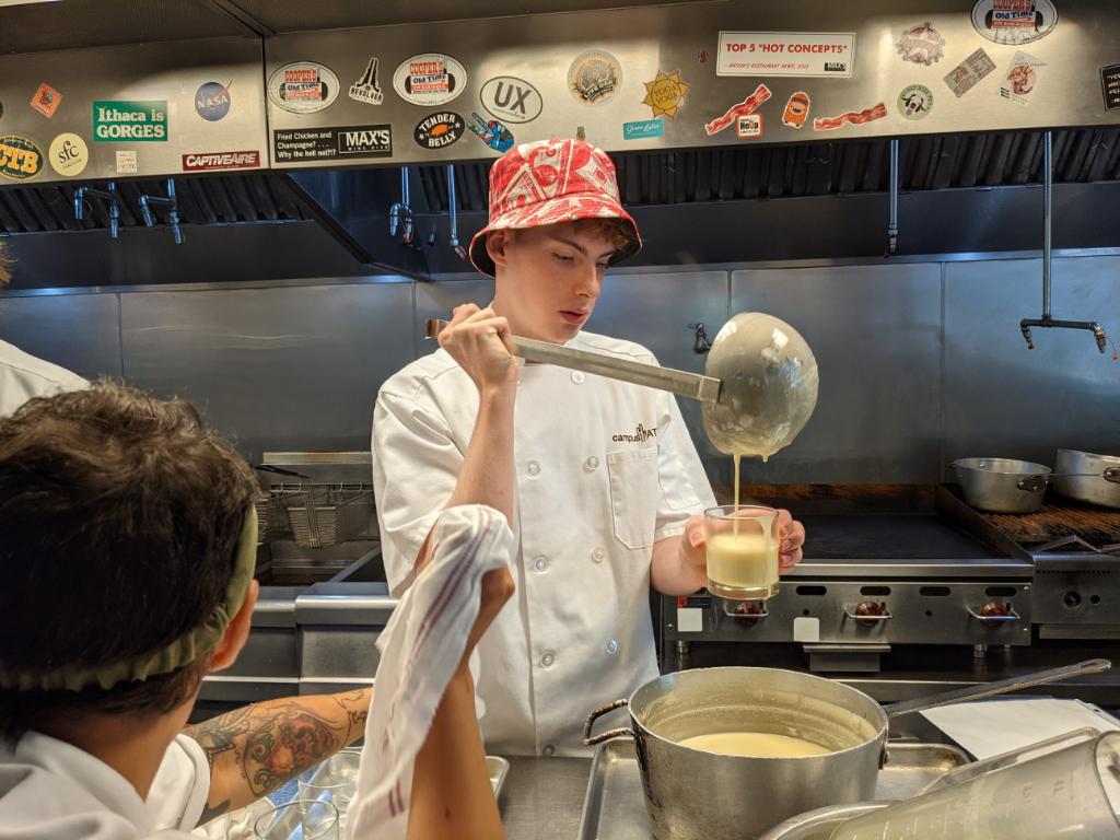 Teen camper in chef coat carefully pouring sauce in a professional kitchen